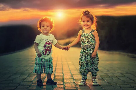 Two children standing hand in hand in front of a sunset